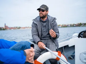 Mann sitzt im Boot, spricht mit Passagieren, Wasserlandschaft.