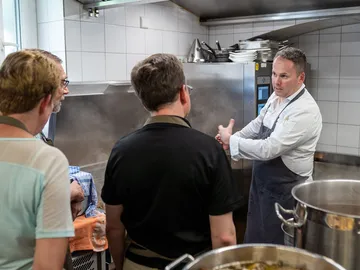Chef explains cooking technology to interested listeners in the kitchen.
