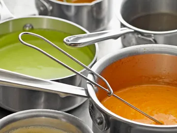 Several metal pots with colorful soups on a table.