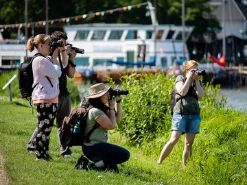 Four photographers hold cameras on the banks of a body of water.