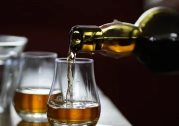 Eine Flasche gießt einen goldenen Drink in ein Glas.