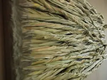 A braided broom stands on a wooden wall.