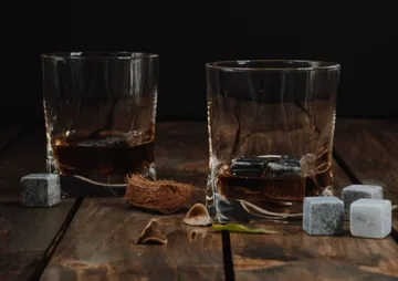 Zwei Gläser mit Whisky stehen auf holzfarbenem Tisch.