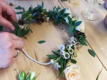 Eine Person bindet einen Kranz aus Blumen und Blättern.