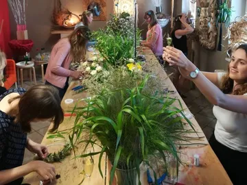 Frauen gestalten Blumenarrangements an einem langen Tisch.