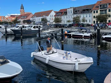 A boat sails between other boats in the harbor.