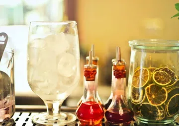 A glass of ice is placed next to various syrup bottles.