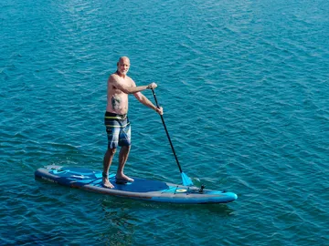 Man paddles on a board in blue water.