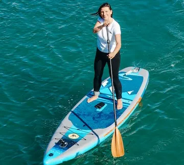 Woman stands on stand-up paddle board and paddles in water.