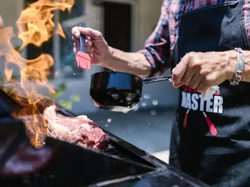 Meat is spread with sauce on the grill, flames burn.