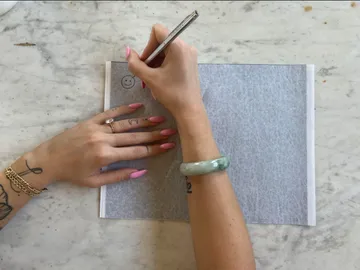 Hands draw on gray paper on a table.