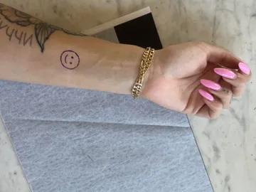 Arm with smiley face and pink nails on grey table.