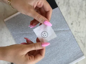 Hands hold a note with a smiley face over it.