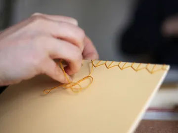 Eine Hand näht gelbes Garn durch einen braunen Umschlag.
