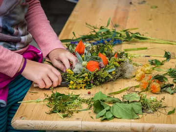 Child ties a wreath of flowers on a table.