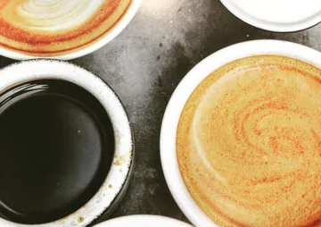 Tassen mit verschiedenen Kaffeesorten auf einer dunklen Oberfläche.