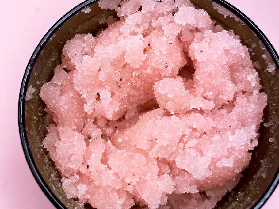 Pink body scrub in a black bowl on a pink background.