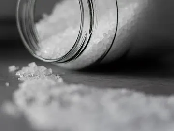 A glass of salt is tilted on a surface.