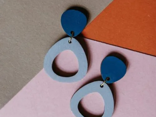 Colourful earrings lie on several layers of coloured paper.