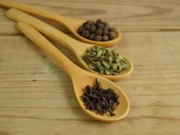 Wooden spoons hold various spices on wooden surfaces.