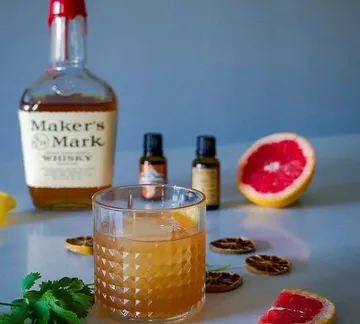 Whiskey glass with drink surrounded by fruits and oils.