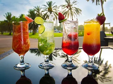 Vier bunte Cocktails stehen auf einem Tisch im Freien.