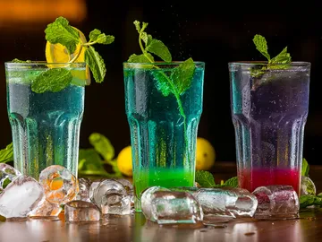 Three colorful cocktails with ice cubes and mint.