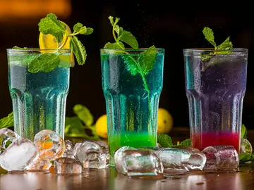 Bunte Getränke stehen mit Eiswürfeln auf einem Tisch.