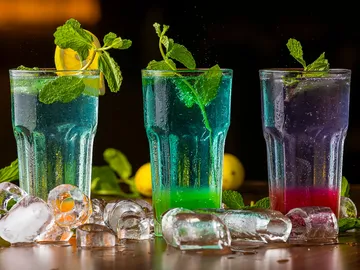 Bunte Cocktails in Gläsern, umgeben von Eiswürfeln.