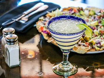 Cocktail glass with margarita stands in front of a colorful dish.
