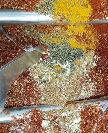 Gemischte Gewürze liegen auf Metalloberfläche, werden geschaufelt.