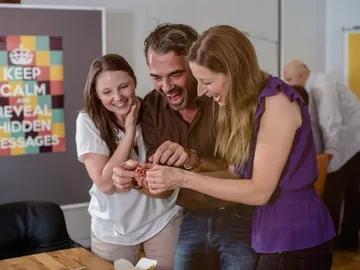 Drei Personen zeigen Freude beim gemeinsamen Entdecken eines Objekts.