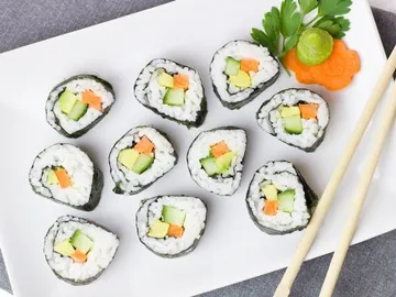 Sushi rolls lie on a white plate with chopsticks.