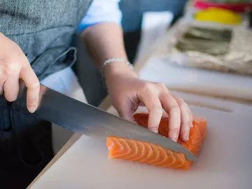 One hand cuts salmon on a cutting board.