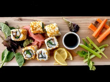 Sushi rolls are laid out on a wooden board with vegetables and soy sauce.