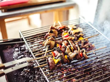 Grill skewers on a rack surrounded by smoke.