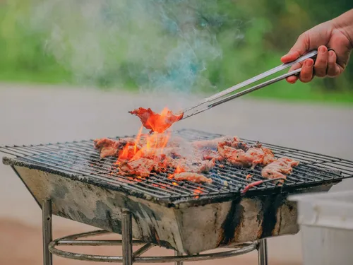 Grill with fire; someone rotates the meat outdoors.