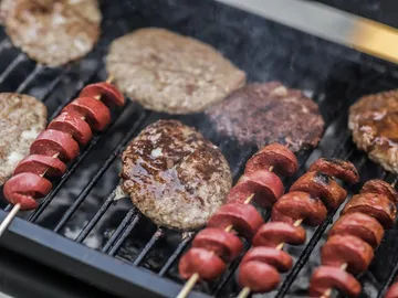 Gegrillte Burger und Spieße auf rauchendem Grillrost.
