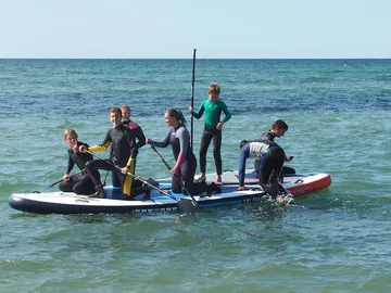 Groups of kids happily paddle on a stand-up paddleboard.