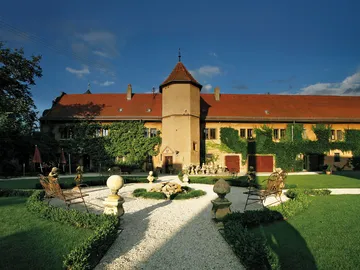 Fassade eines historischem Gebäudes umgeben von Gartenmöbeln.