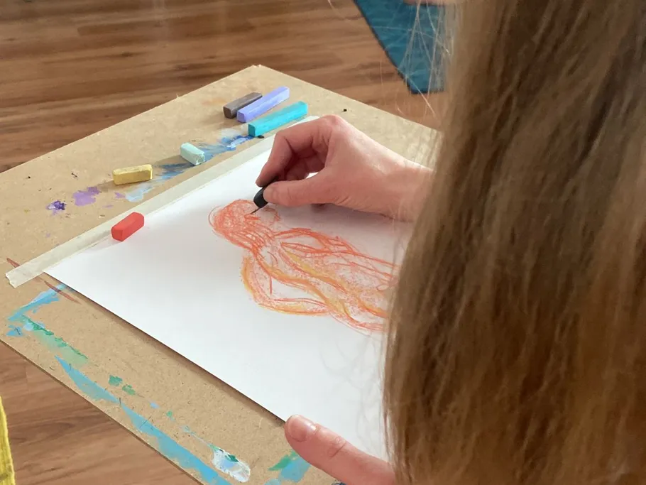 A hand draws a figure on paper with chalk.