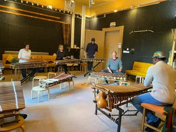 Sechs Personen spielen gewichtete Musikinstrumente in einem Raum.