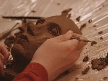 Ein händisches Modellieren einer Tonfigur auf einer Arbeitsfläche.