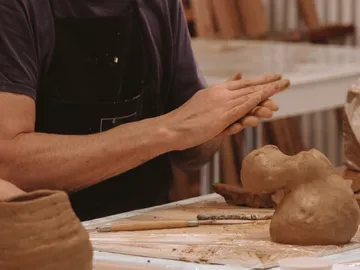 Tonfigur wird von Händen im Atelier geformt und bearbeitet.