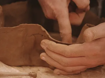 Hands form clay in a creative workshop environment.