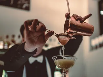 Cocktailshaker gießt Getränk durch Sieb in Glas.