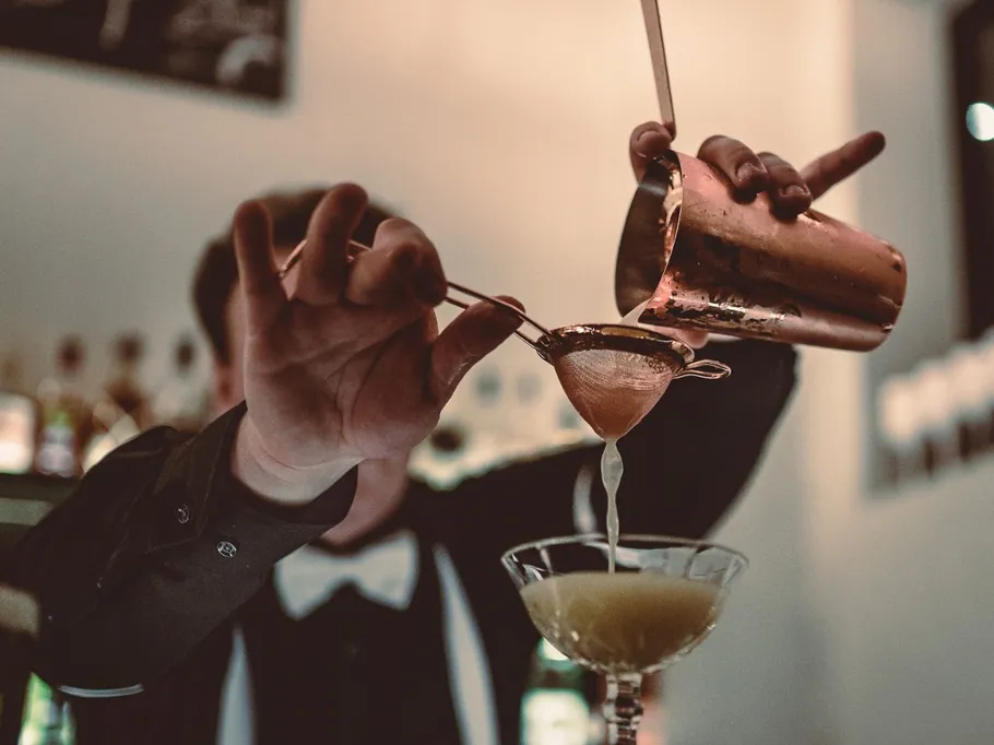 Cocktailshaker gießt Getränk durch Sieb in Glas.