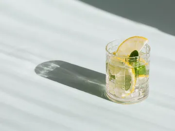 A glass with lemons and mint stands on a surface.