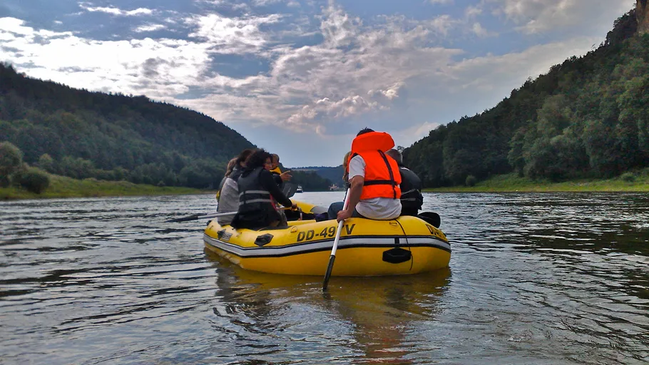 Rubber boat sails on calm water between wooded shores.