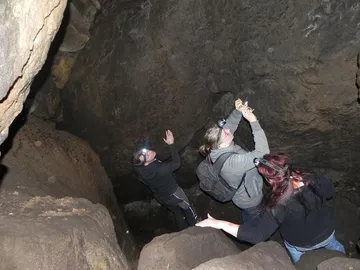 Three people explore a cave wearing helmet lamps.